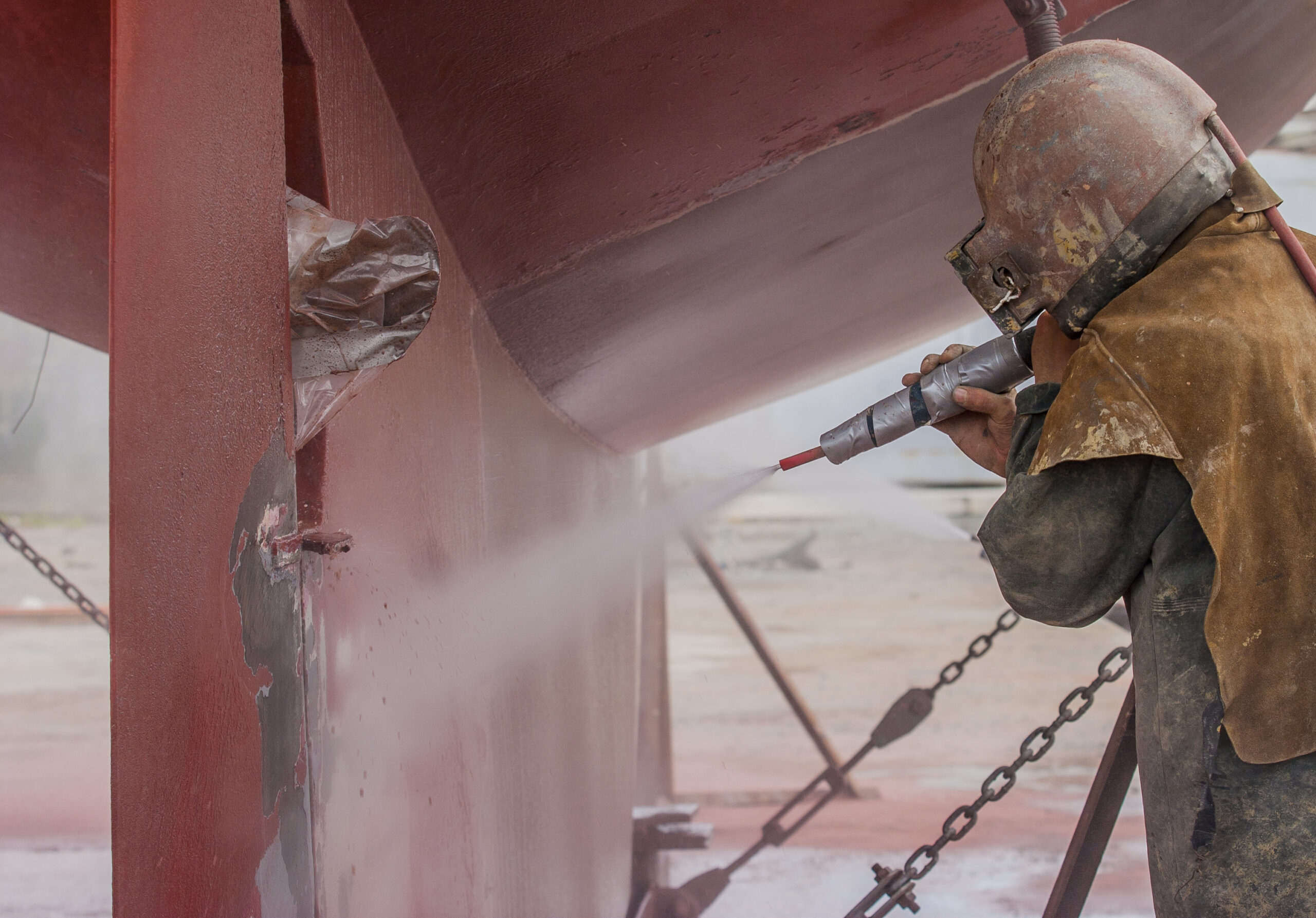 Worker performing industrial sandblasting on a corroded hull